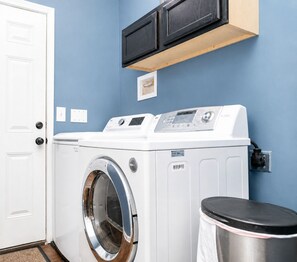 Une buanderie équipée d’un lave-linge et d’un sèche-linge à chargement frontal, d’une poubelle et d’une prise électrique murale.