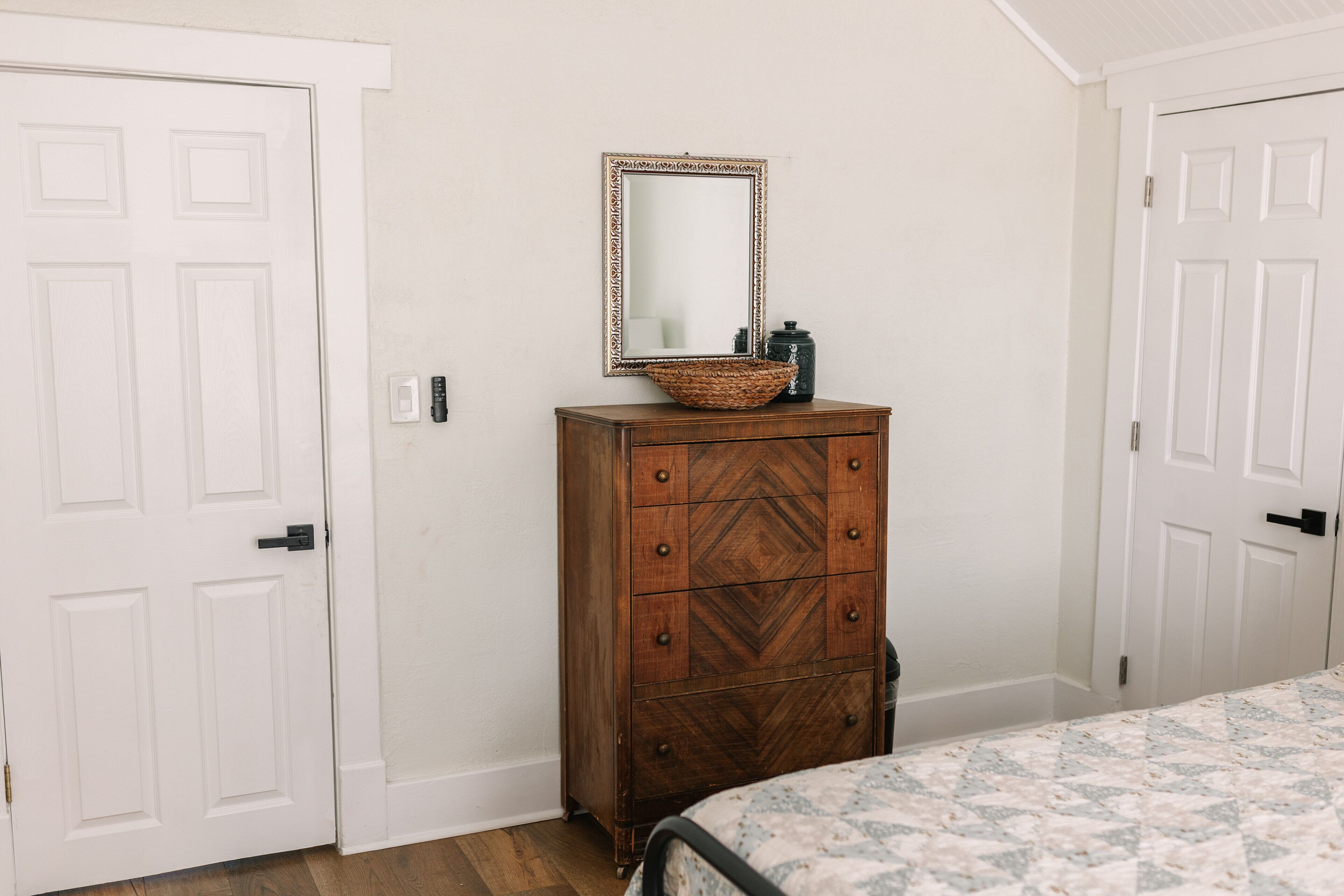Une chambre à coucher avec une commode en bois, un miroir et un lit recouvert d’une couvre-lit à motifs.