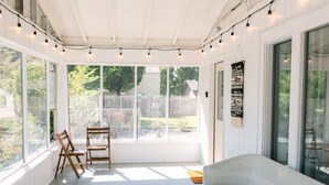 A sunlit room with large windows, a wooden floor, a cushioned bench, and string lights. - The Kennewick Cottage  (Kennewick)