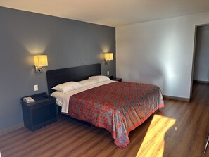 A neatly made bed with a patterned bedspread, two bedside lamps, a nightstand with a phone, and a wooden floor.