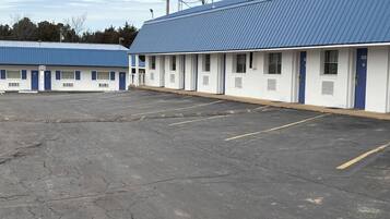 Un motel con un amplio estacionamiento y una hilera de habitaciones con puertas azules.