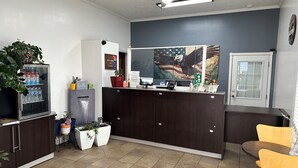 A reception area with a dark wooden counter, a water dispenser, potted plants, and a large window with an eagle mural. - Motel 6 Sullivan, MO (Sullivan)