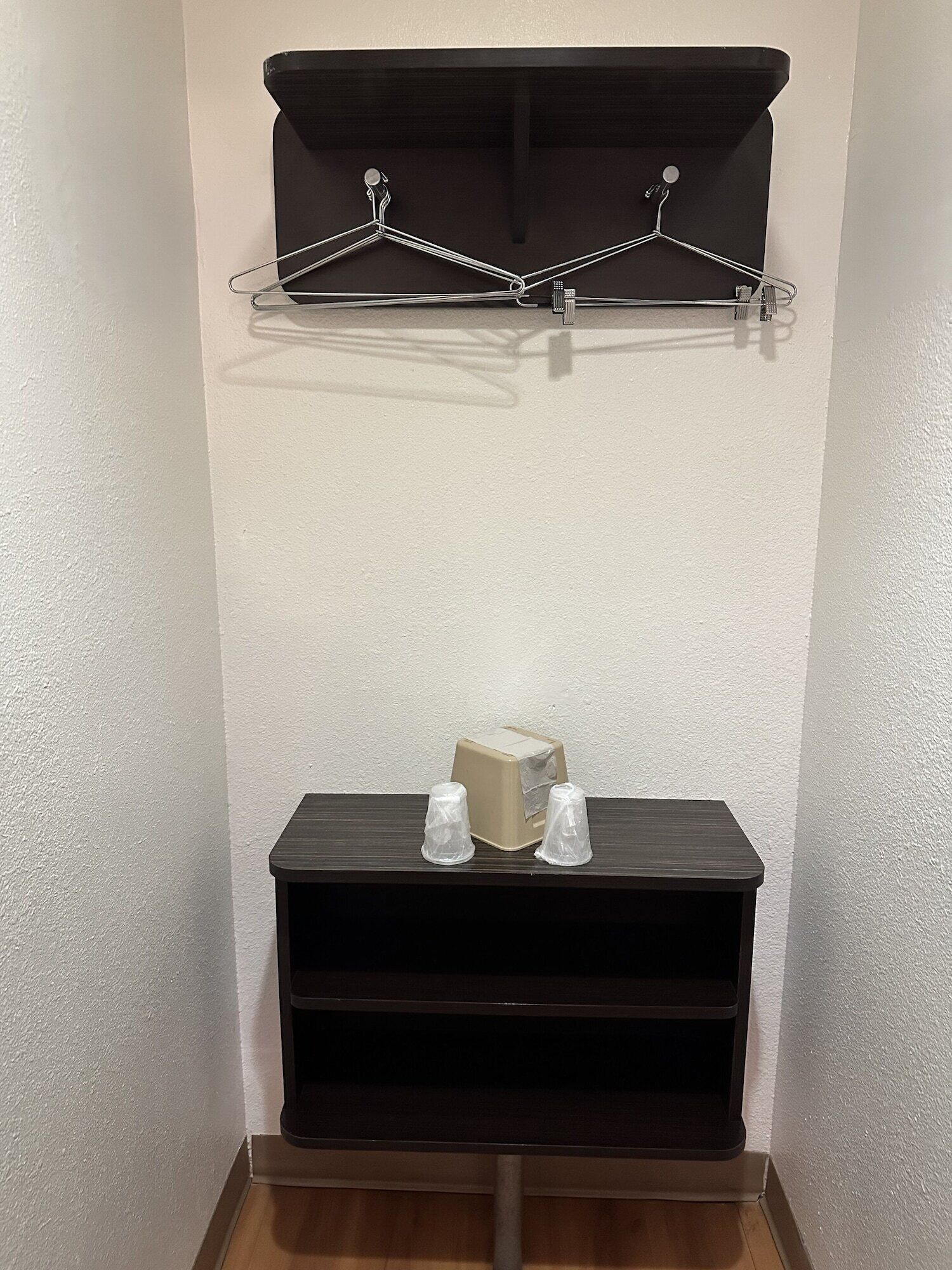 A corner with a dark wooden shelf, two clear plastic cups, and a beige box.