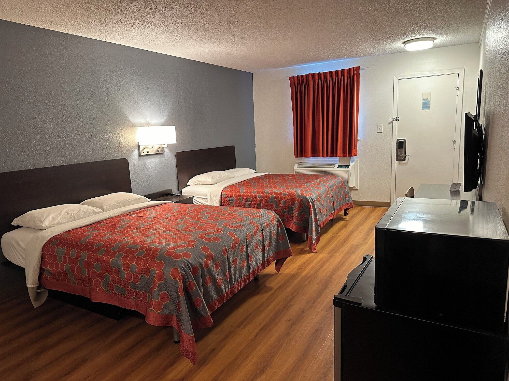 Una habitación de hotel con dos camas, un escritorio, un televisor y una ventana con cortinas rojas.