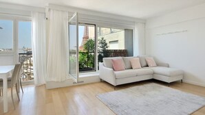 A modern living room with a white sofa, a dining table with chairs, and a large window offering a view of the Eiffel Tower. - Top Floor Eiffel Tower View and High-speed Wi-Fi (Paris)