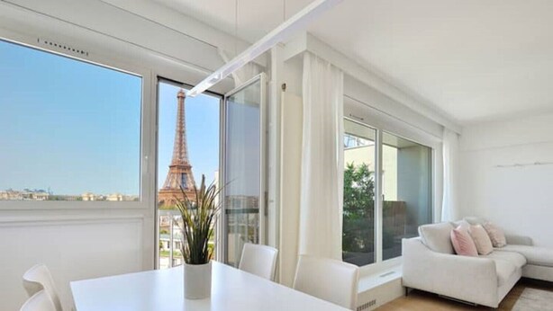A modern apartment with a dining area, a sofa, and a view of the Eiffel Tower. - Top Floor Eiffel Tower View and High-speed Wi-Fi (Paris)