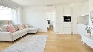 A modern living room with a light-colored sofa, a grey rug, and a kitchen area with white cabinets and a built-in oven. - Top Floor Eiffel Tower View and High-speed Wi-Fi (Paris)
