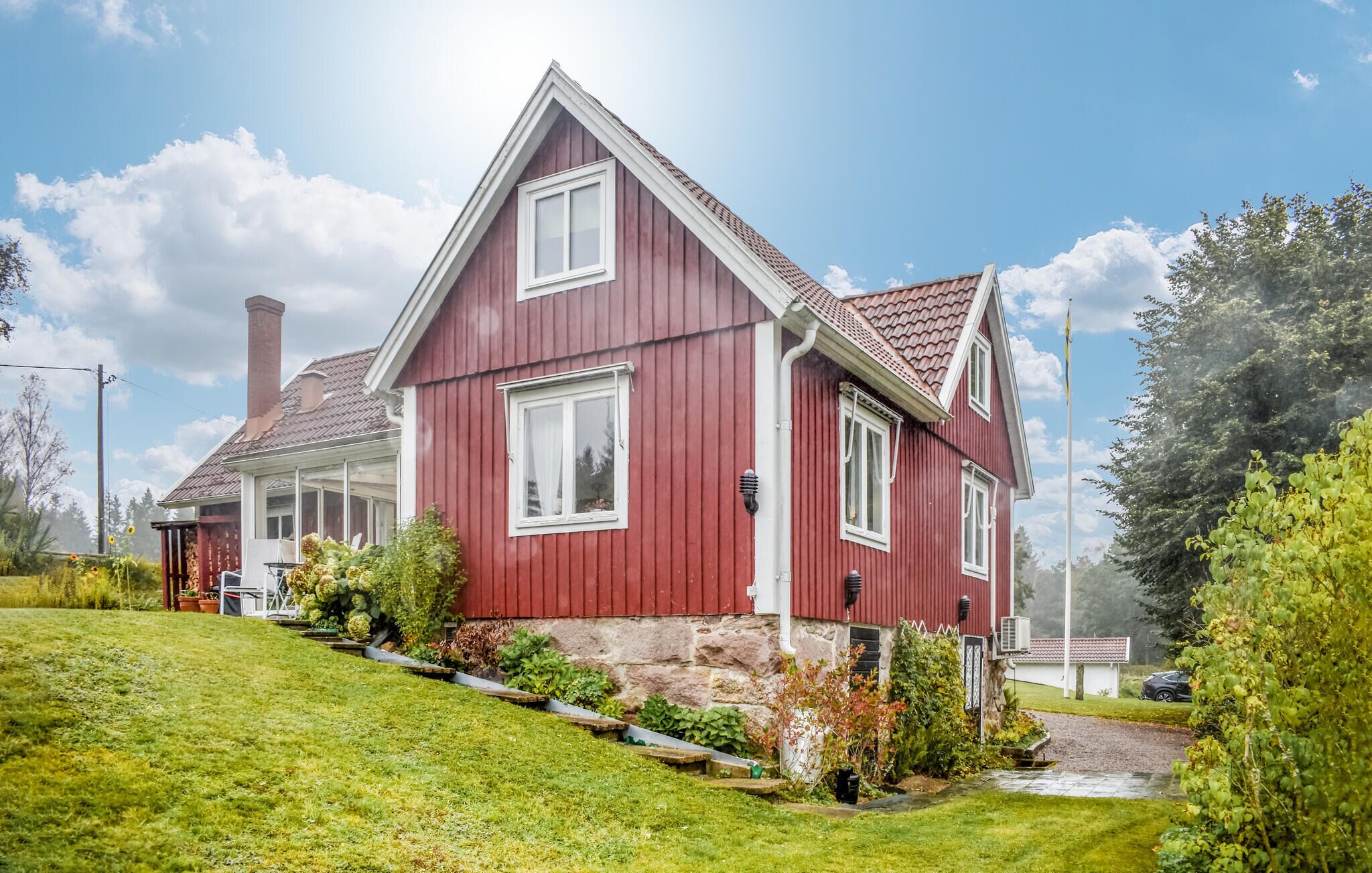 Et rødt hus med to etager, skråt tag, skorsten og en velplejet græsplæne.