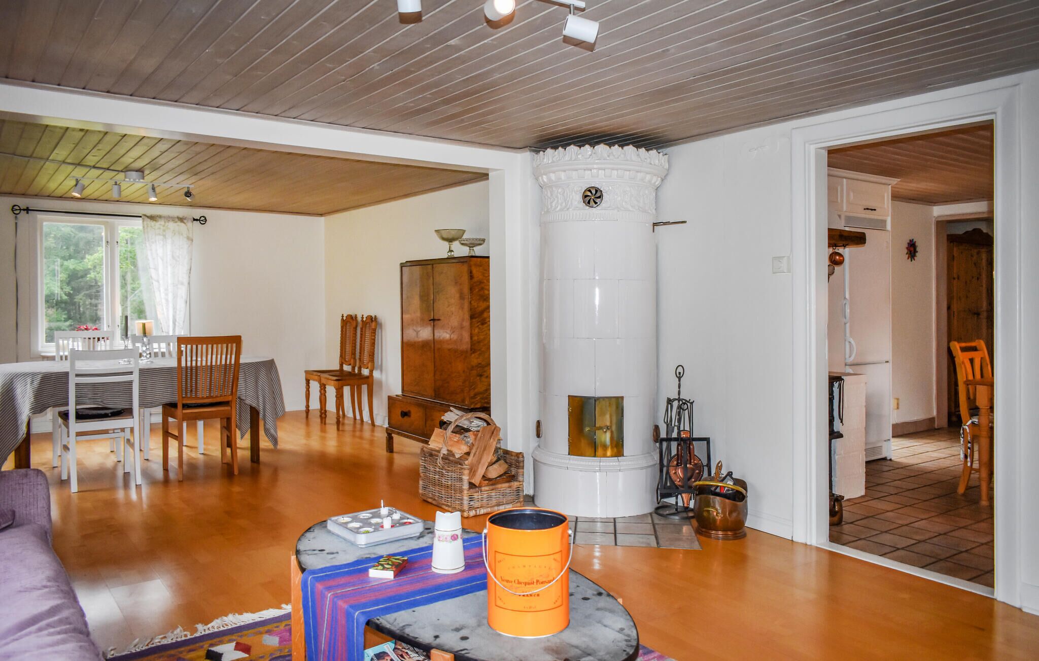 Un salon chaleureux avec un plancher en bois, un coin repas avec une table et des chaises, une cheminée et une vue sur l’extérieur par une fenêtre.