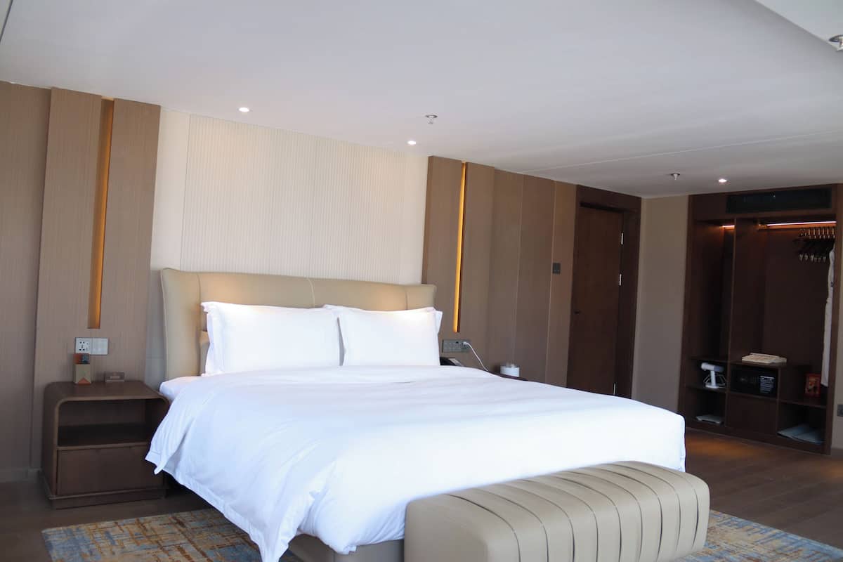 Ett modernt hotellrum med en stor säng, ett sängbord, en liten avlastningsyta, en bänk och en garderob.