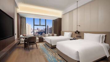 A hotel room with two beds, a desk, a chair, and a large TV.