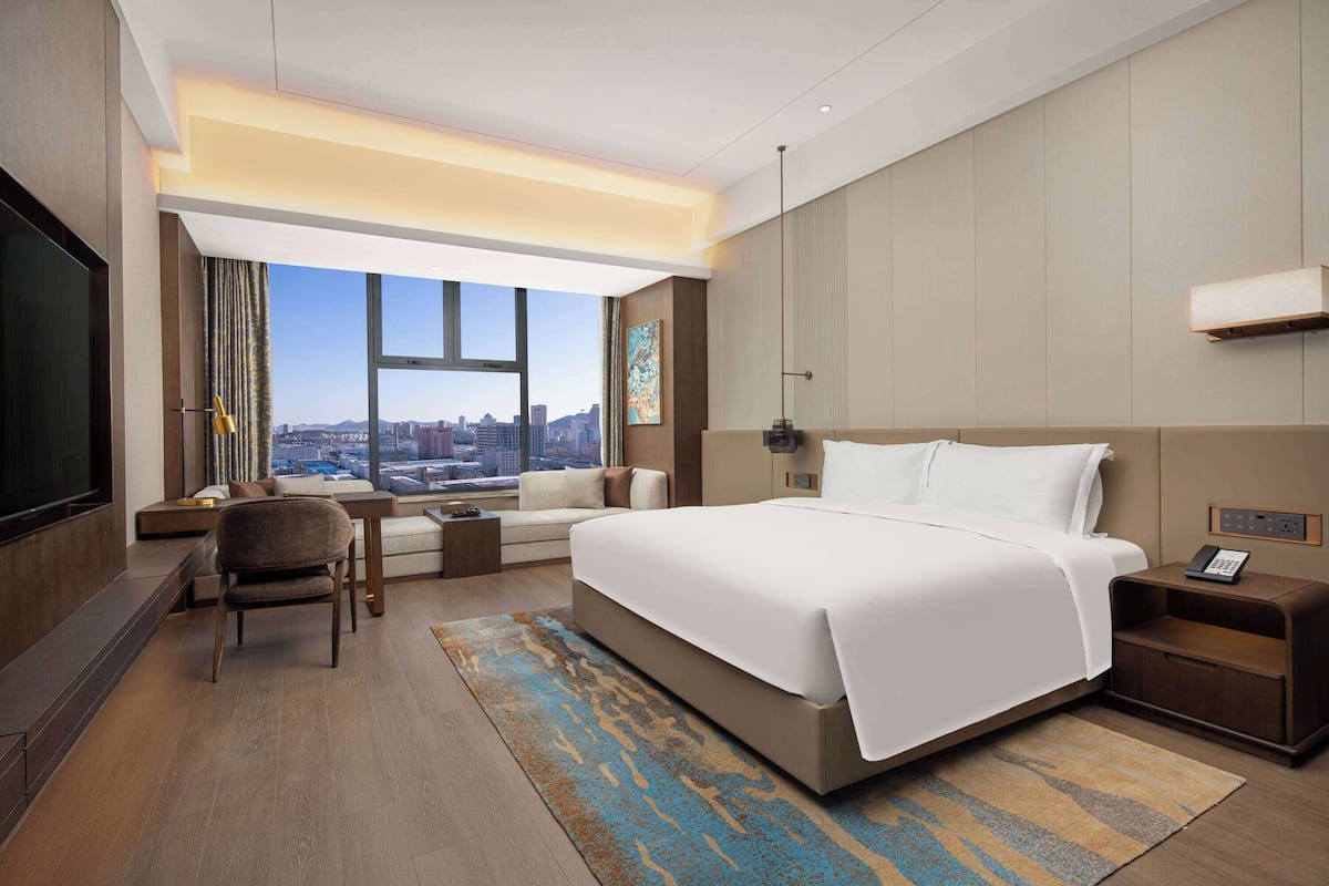 Ett modernt hotellrum med en stor säng, en soffa, ett skrivbord och utsikt över staden.
