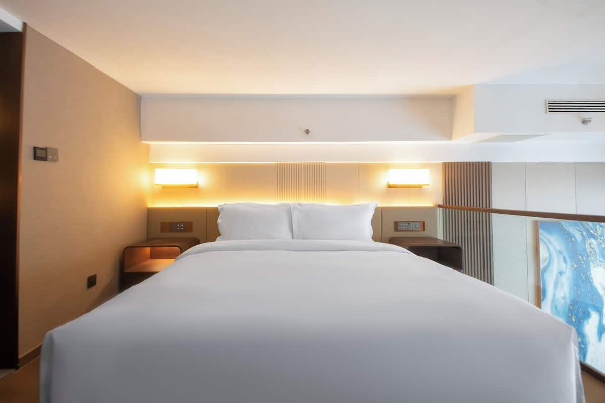 Ett modernt hotellrum med en stor säng, två sängbord och väggmonterad belysning.