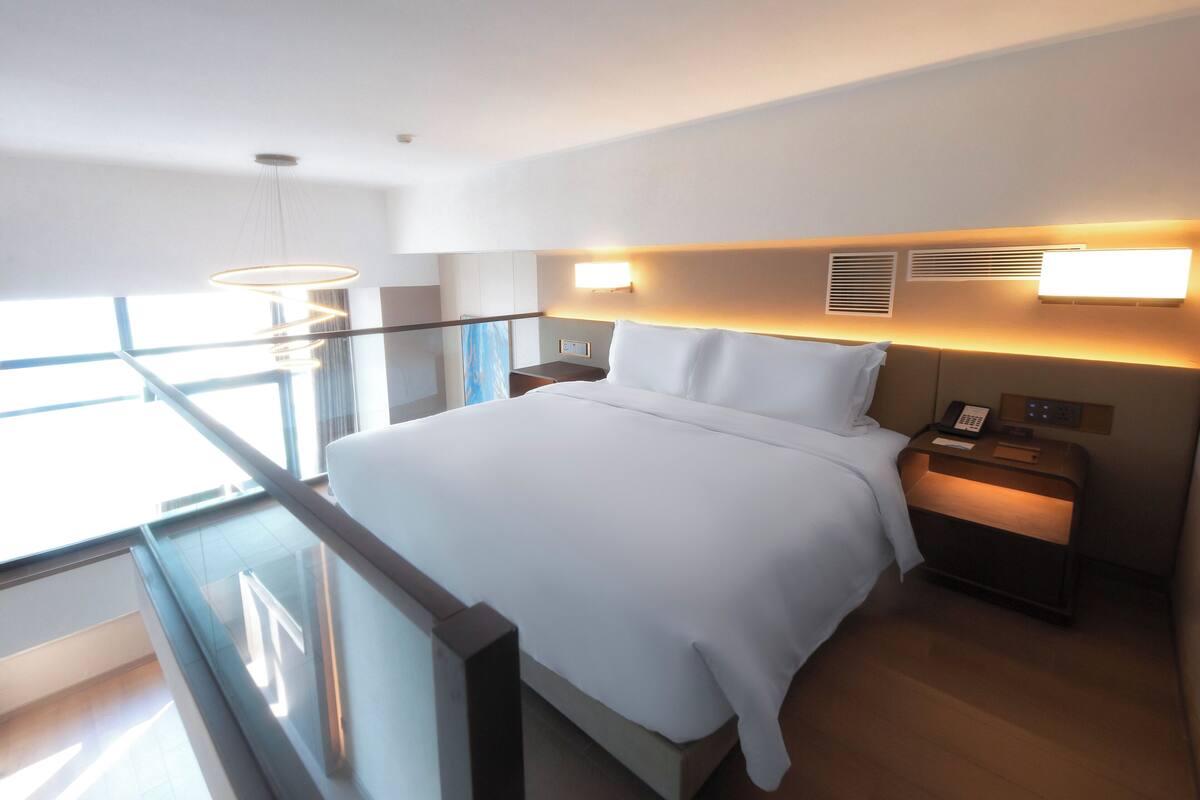 Ett modernt hotellrum med en stor säng, sängbord, ett litet bord med en telefon och utsikt över omgivningarna från balkongen.