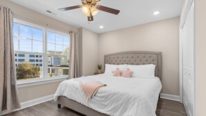 Une chambre avec un grand lit, un ventilateur de plafond et une vue sur les maisons voisines.