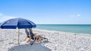 Eine Strandansicht mit einem blauen Sonnenschirm und einem Holzliegenstuhl.