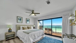 A bedroom with a bed, a nightstand, a ceiling fan, a large window, and a view of the ocean. - Gulf Front Luxury-Ocean View Suites! Private Beach (Destin)
