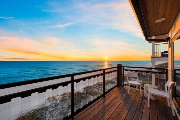 A wooden deck with a railing overlooking the ocean at sunset.