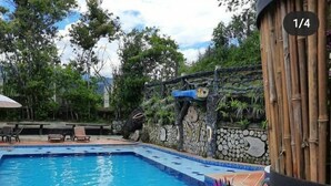 A pool area with a person relaxing on a lounge chair, surrounded by purple flowers. - Finca hotel Sendero del rio (San Rafael)