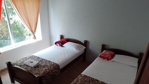 Two single beds with patterned bedspreads, a window with curtains, and a wooden floor. - Finca hotel Sendero del rio (San Rafael)