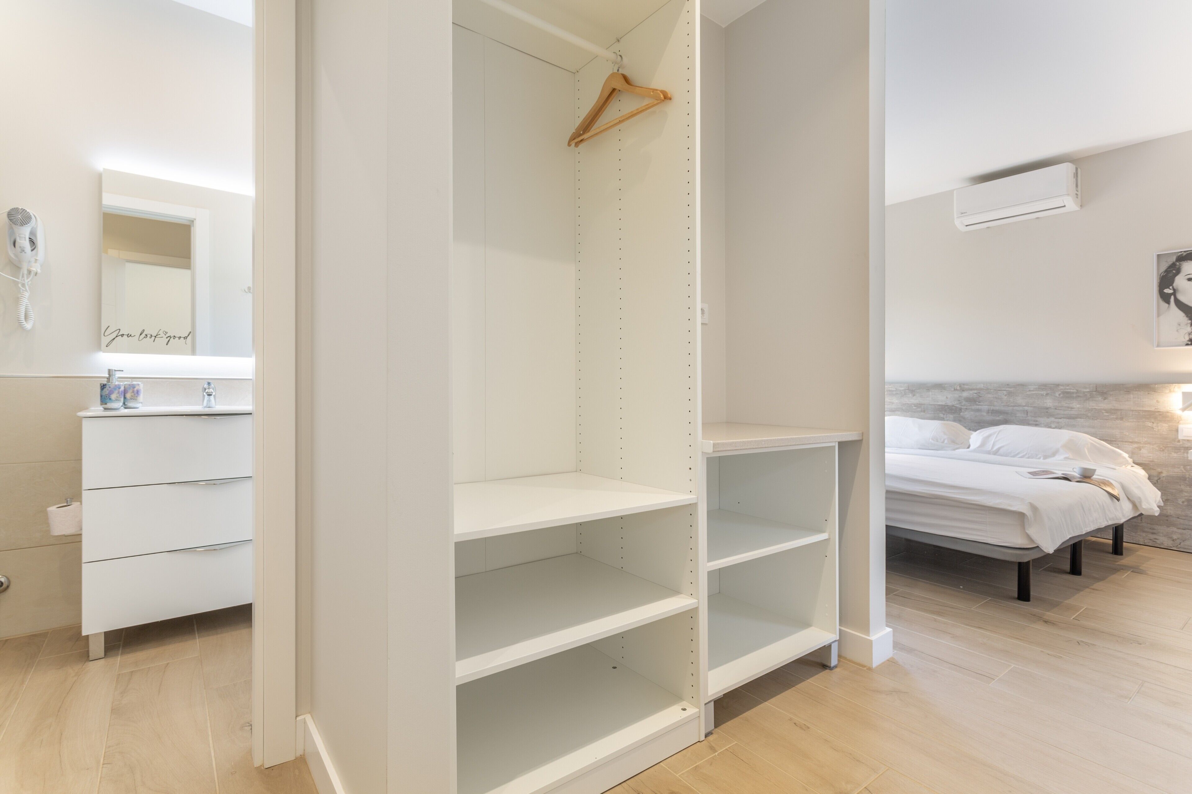 Un dormitorio con una cama, un armario blanco, un espejo y una percha para ropa.