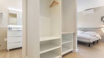 Un dormitorio con una cama, un armario blanco, un espejo y una percha para ropa.