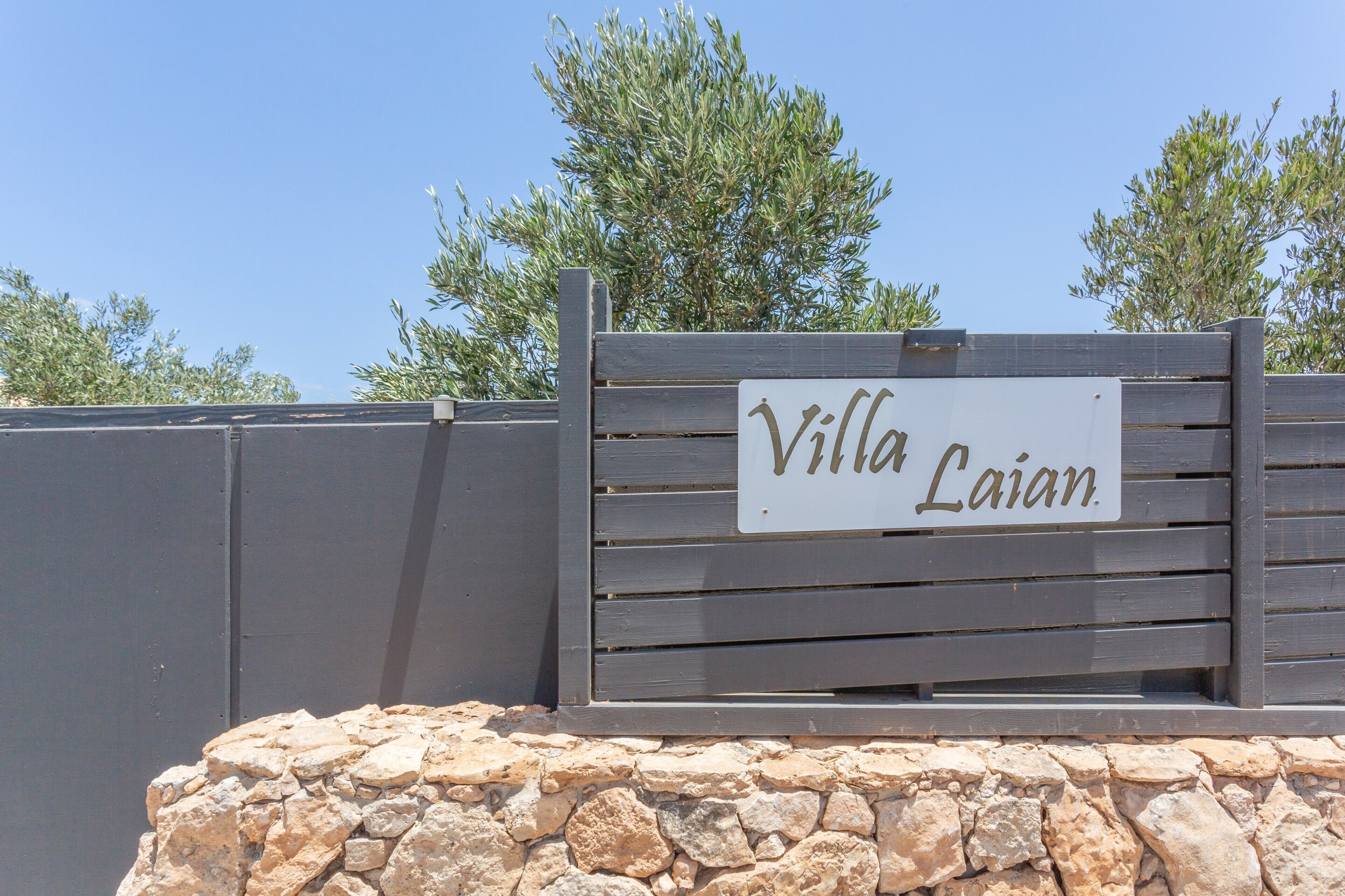 Un letrero de madera con el texto 'Villa Laian' sobre un muro de piedra.