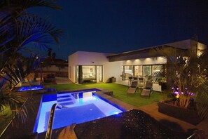 Une maison moderne dotée d’une piscine, de mobilier d’extérieur et d’un intérieur bien éclairé.