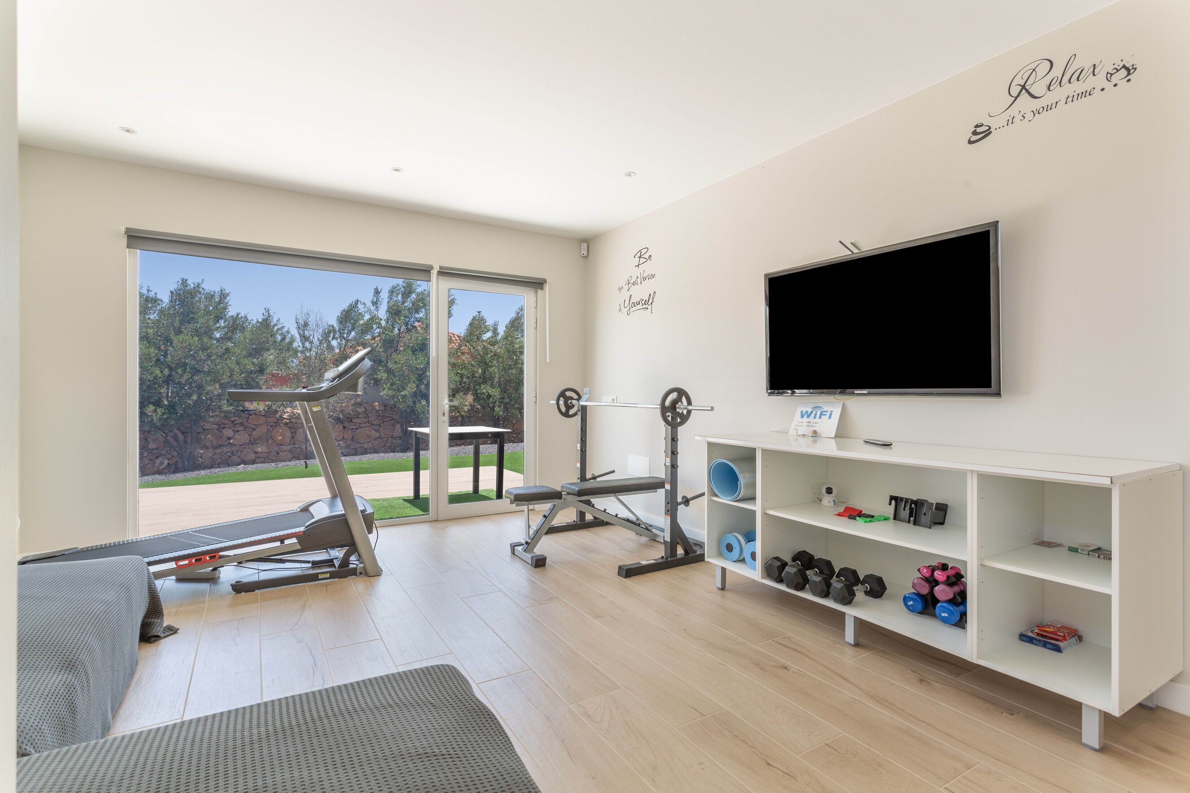 Een moderne sportschool thuis met trainingsapparatuur, een televisie en uitzicht op de omgeving.