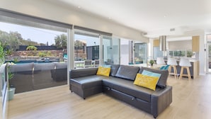 A modern living room with a sectional sofa, a dining area, and a kitchen. - Laian Branded Residensed House with Private Pool and Air Conditioning (Triquivijate)