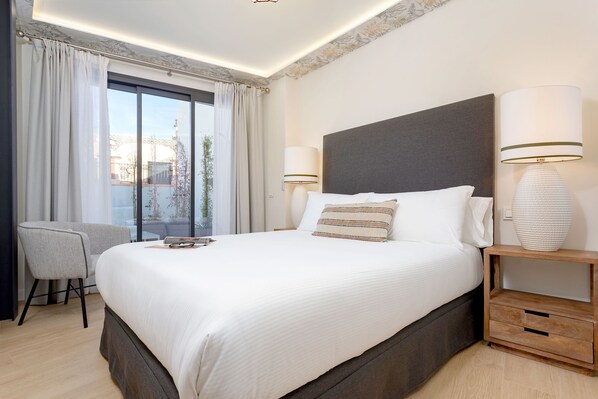 A modern hotel room with a large bed, a chair, a bedside table with a lamp, and a view of the city through the window.