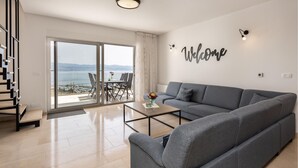 Un salon spacieux avec un canapé gris, une table basse et une vue sur la mer grâce à de grandes fenêtres.