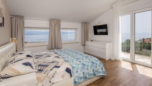 Une chambre à coucher avec un lit, une télévision, une commode et une grande fenêtre donnant sur la mer.