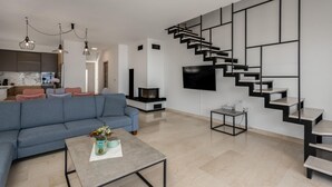 Un salon moderne avec un canapé bleu, une table basse, un téléviseur et un escalier noir.