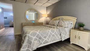 A bedroom with a bed, a bedside table, a lamp, a mirror, and a small plant. - Lux Utica Retreat  (Utica)