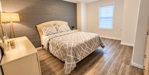 Een slaapkamer met een bed, nachtkastje, lamp en een raam met zonwering.