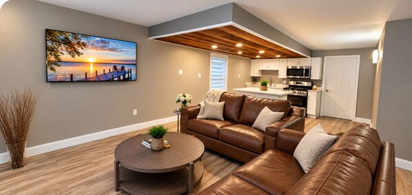 Een moderne woonkamer met een bruine leren bank, een ronde salontafel en een schilderij van een zonsondergang.