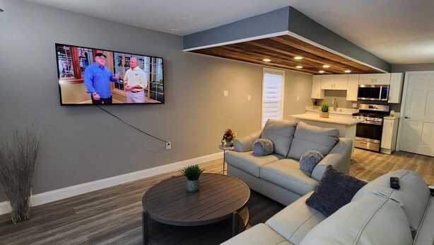 A modern living room with a grey sofa, a round coffee table, and a TV mounted on the wall. - Lux Utica Retreat  (Utica)