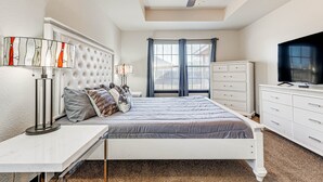 Una camera da letto con un letto, comodini, una ventola a soffitto, una cassettiera e un televisore.