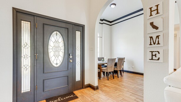 Una porta in legno scuro con un pannello di vetro, un tappetino d'ingresso e un'area pranzo con sedie e tavolo.