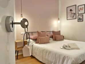 Un dormitorio con cama, almohadas, una mesita de noche y una lámpara colgante.