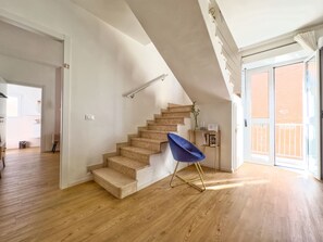A staircase with a blue chair, wooden flooring, and a view of the outside.