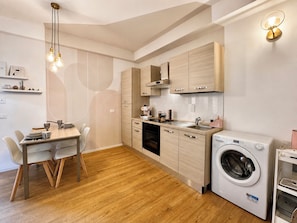 Cocina compacta con muebles de madera, lavadora integrada y zona de comedor con mesa y sillas.