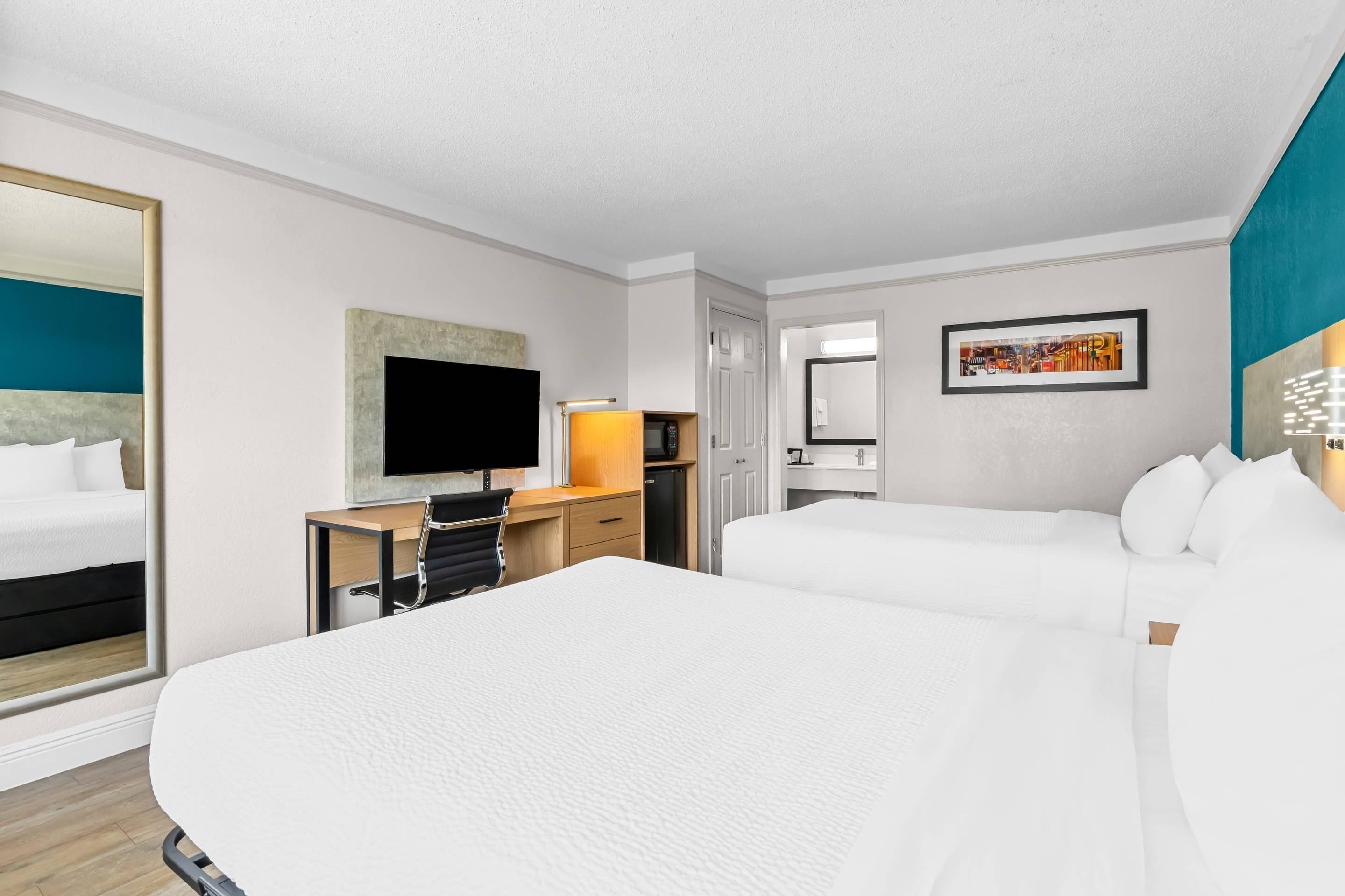 Ein Hotelzimmer mit einem großen Bett, einem Schreibtisch mit Computer, einem Fernseher und einer Tür zu einem weiteren Zimmer.