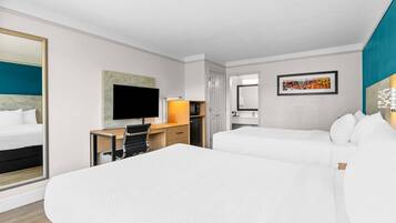 Habitación de hotel con una cama grande, un escritorio con computadora, un televisor y una puerta que da a otra habitación.
