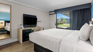 Habitación de hotel con una cama grande, un escritorio con televisor de pantalla plana, un espejo y vistas al exterior.