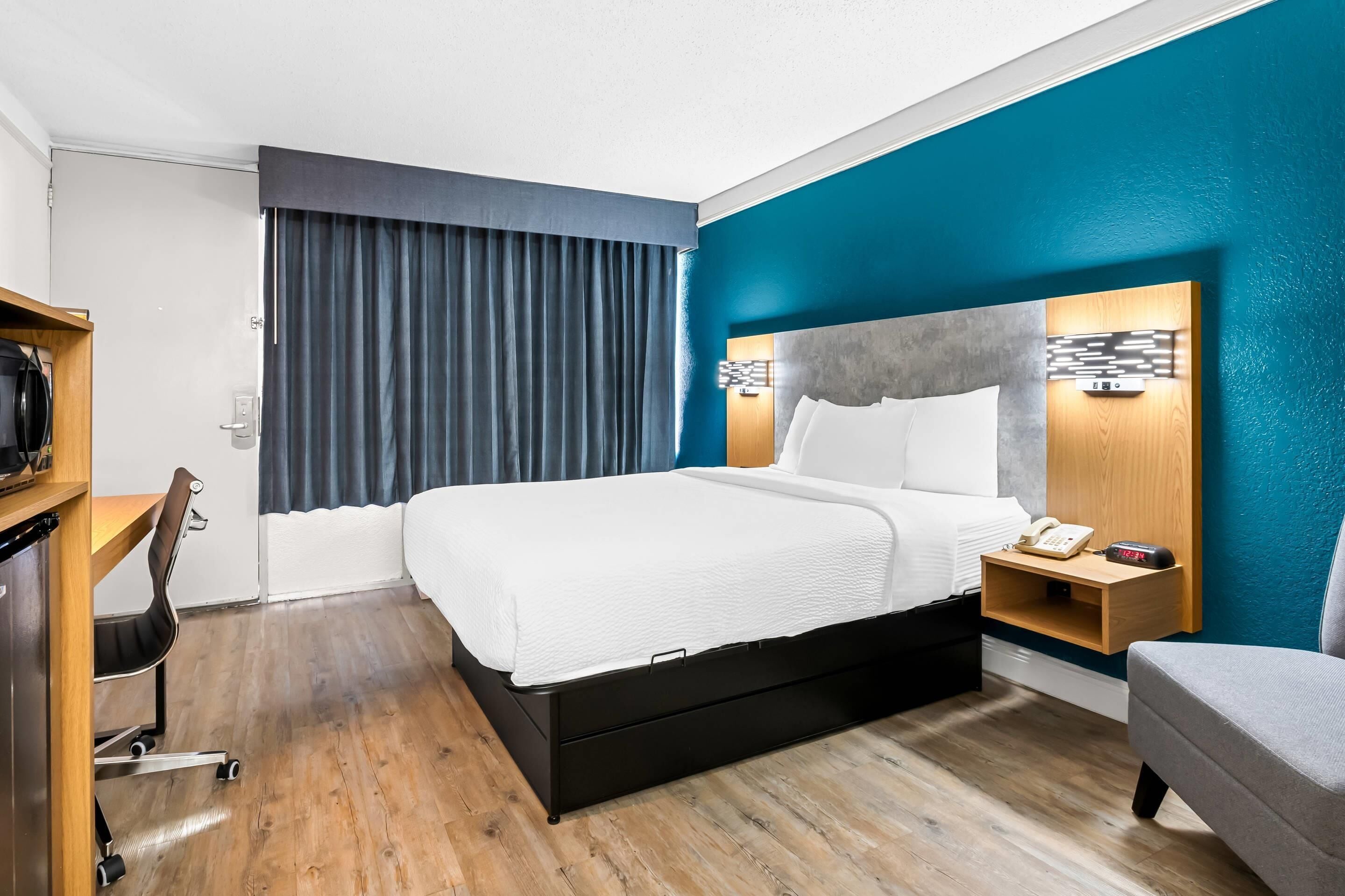 A modern hotel room with a large bed, a desk, a chair, and a TV.