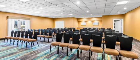 Un salón de conferencias con filas de sillas, una alfombra colorida y un techo blanco con iluminación empotrada.