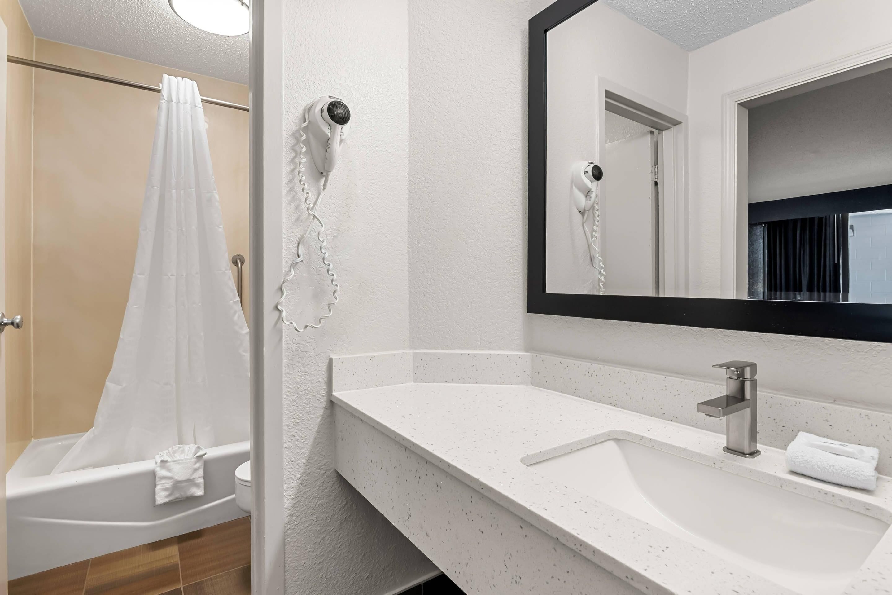 Un baño con un lavabo blanco, un espejo y una ducha con cortina blanca.