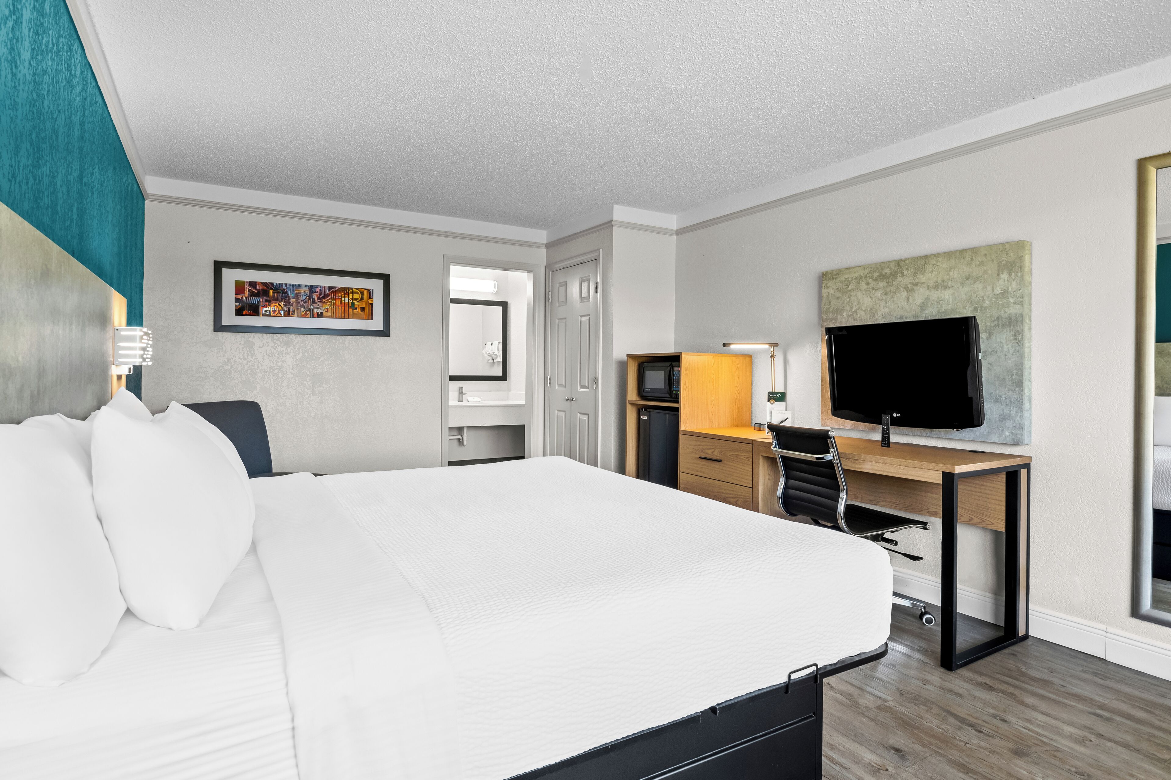 A hotel room with a large bed, a desk with a computer and TV, and a door leading to a bathroom.